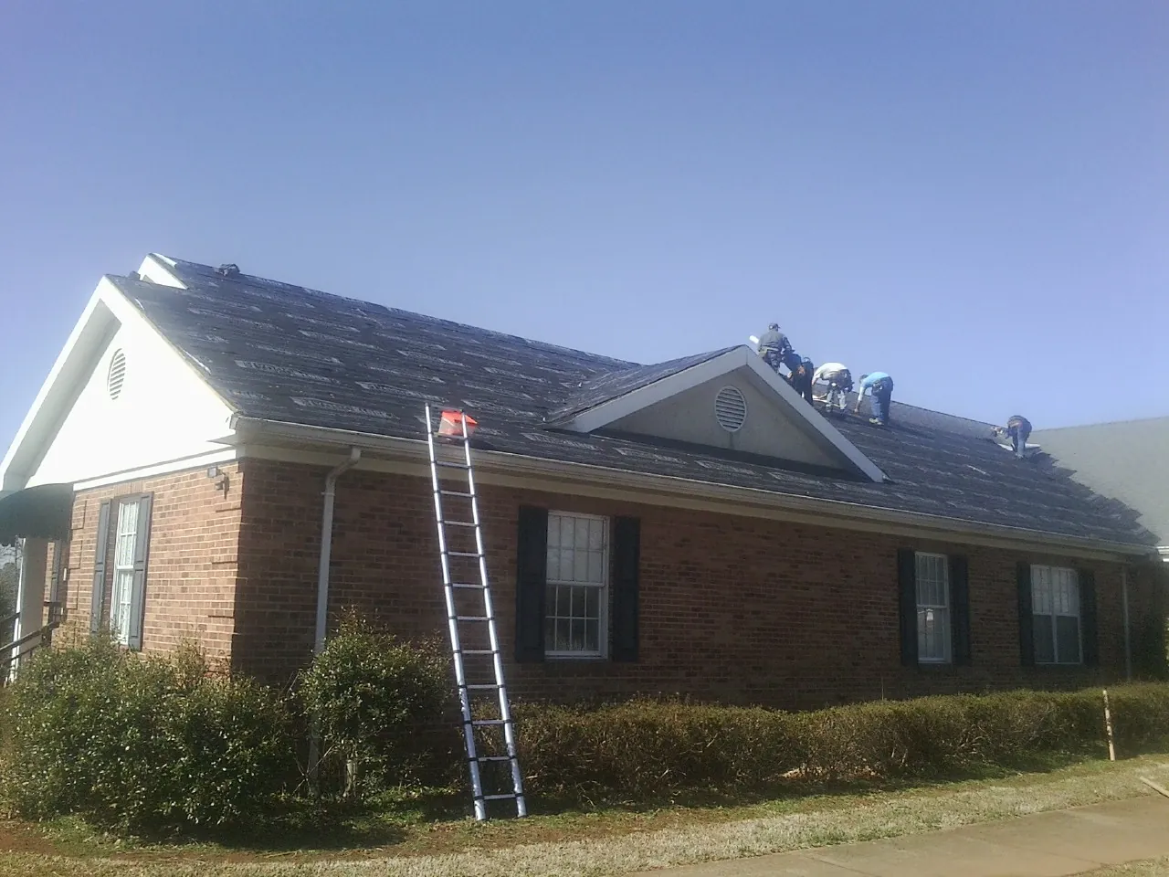 Crew tearing shingles off a brick ranch roof with a ladder set — Emergency Roof Repair work by our crew in Summerfield