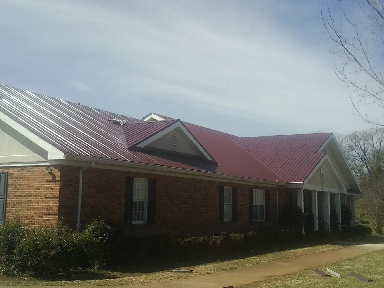 Red metal roof with gabled entries on a long brick building, from a Hail Damage Roof Repair job in Summerfield
