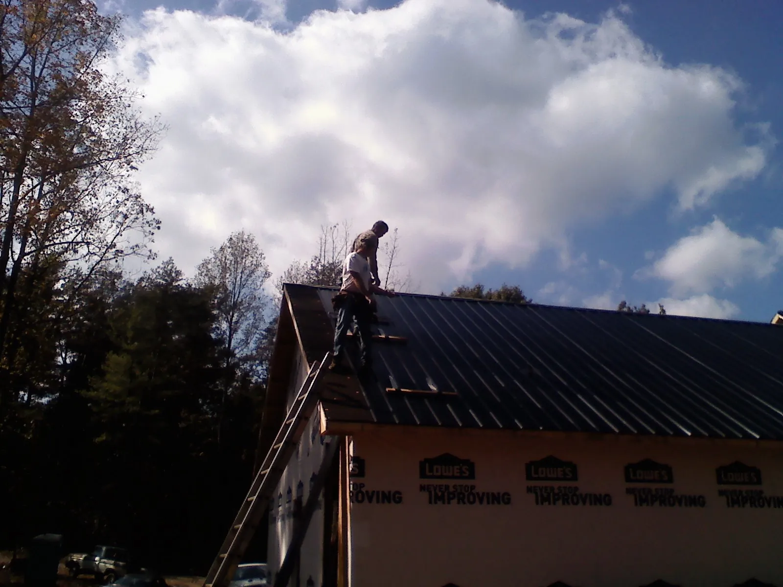 Roofer fastening dark metal panels high against a cloudy sky, from a Roof Inspection job in Summerfield