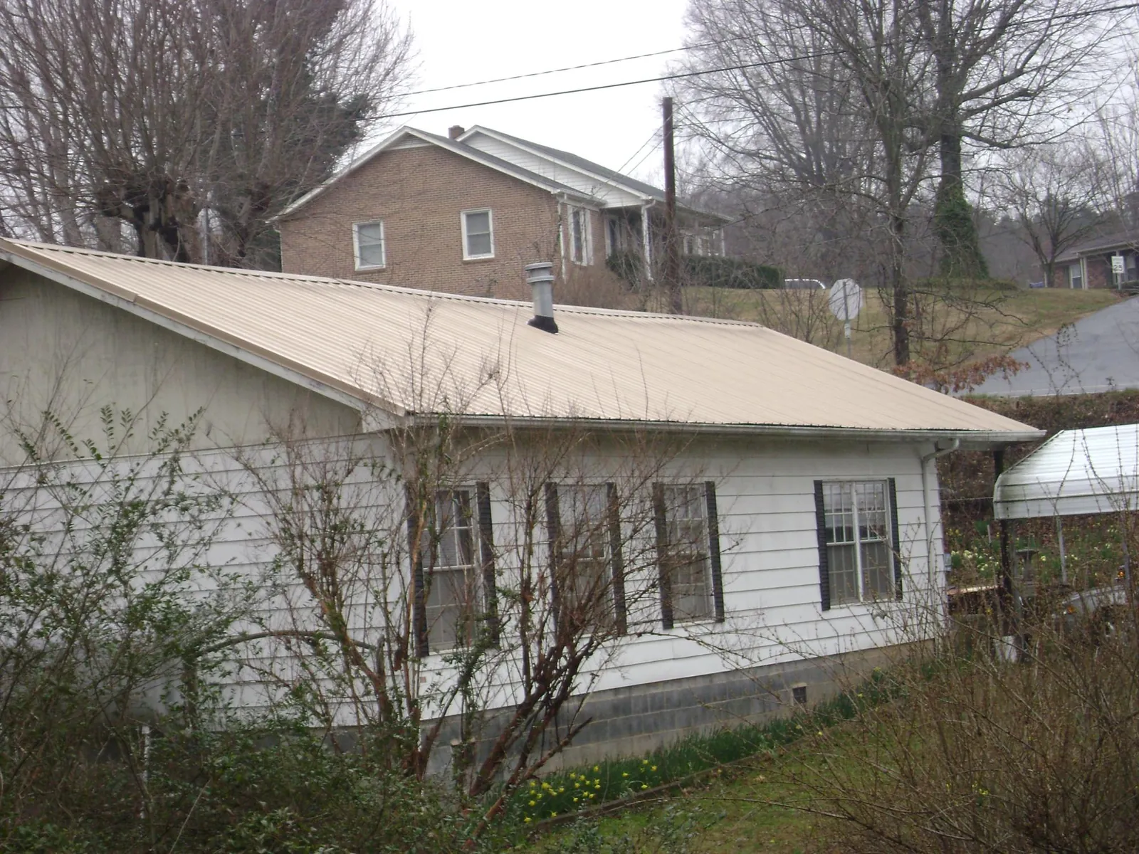 Tan metal roof on a white sided house set into a hillside — Commercial Roofing by Roofing Brothers in Summerfield