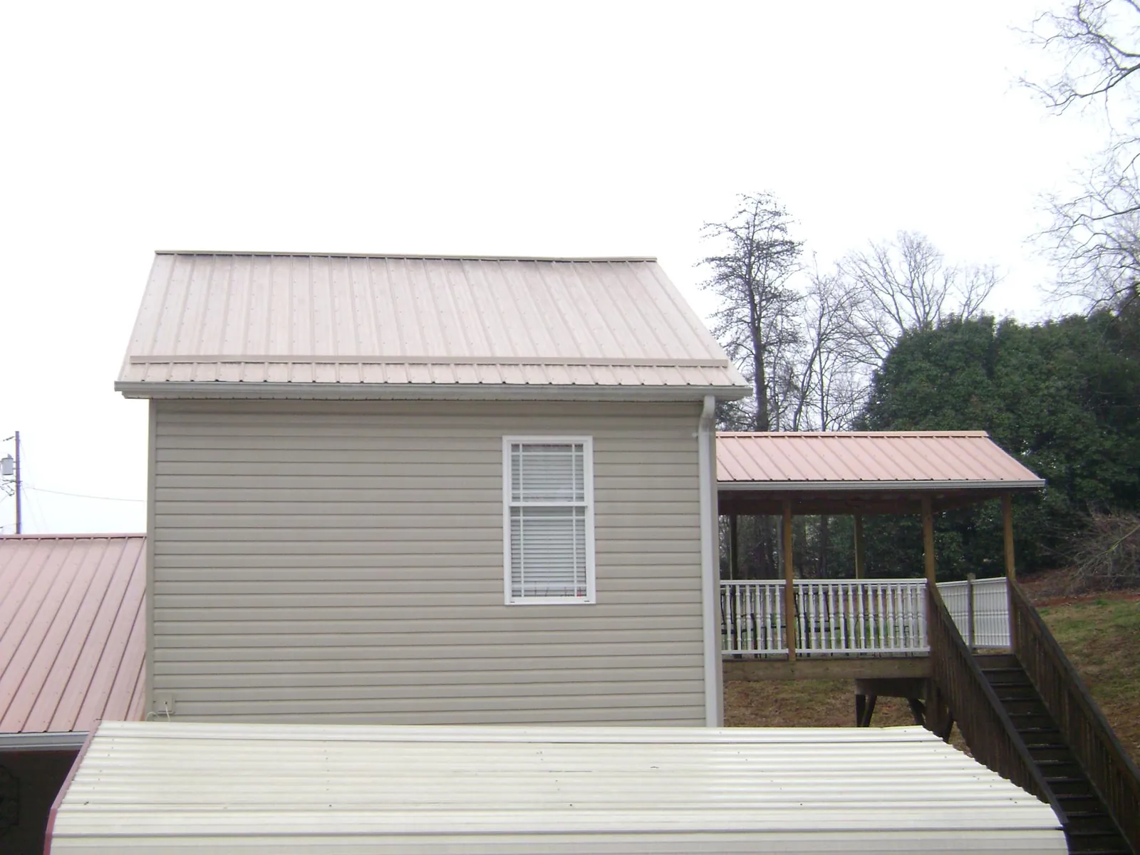 Tan metal roofs on a two story addition and attached porch, from a Roof Replacement job in Summerfield